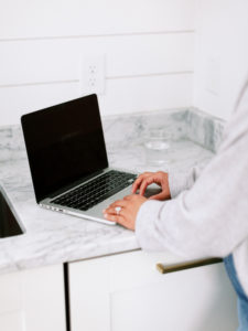 Open laptop on gray marble counter with hands typing.
